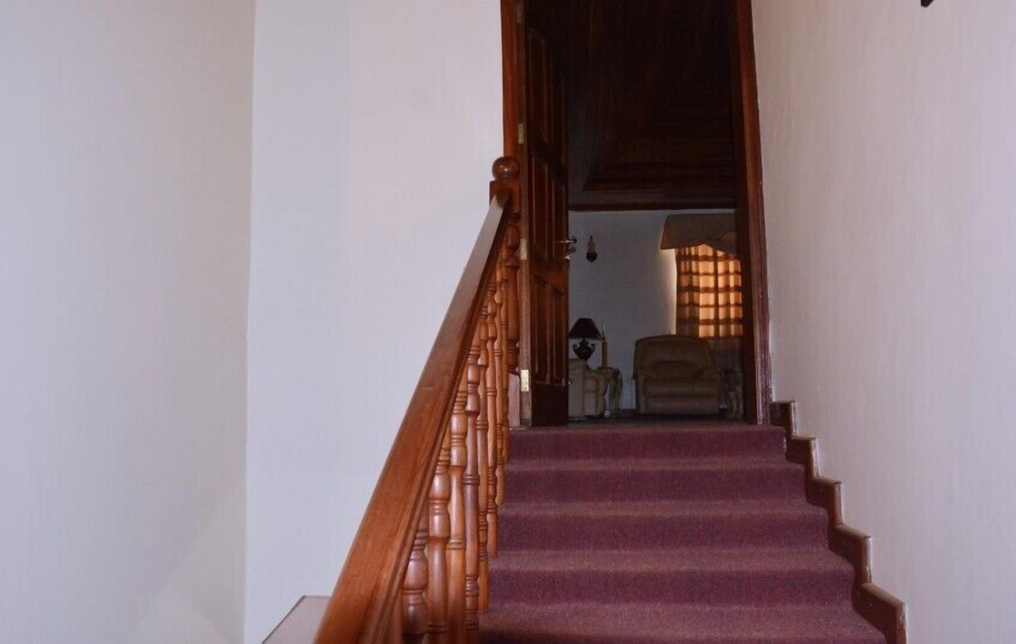 A wooden staircase with a carpeted landing leading to a room with a lamp and a chair.