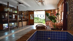 Una habitación con suelo de baldosas, un área con azulejos azules, mobiliario de madera, una pared de ladrillo y vistas al exterior.