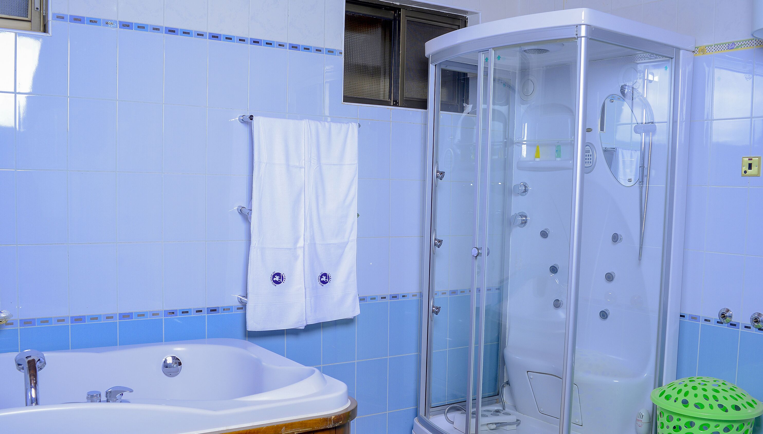 Un baño con bañera, cabina de ducha y un cubo de basura verde.