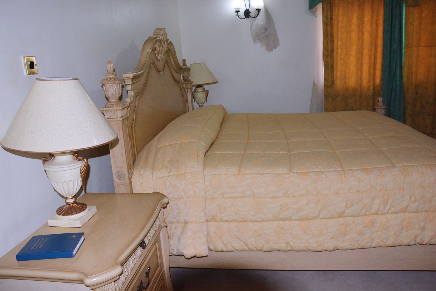 A bedroom with a bed, a nightstand, a lamp, and a wall-mounted light fixture.