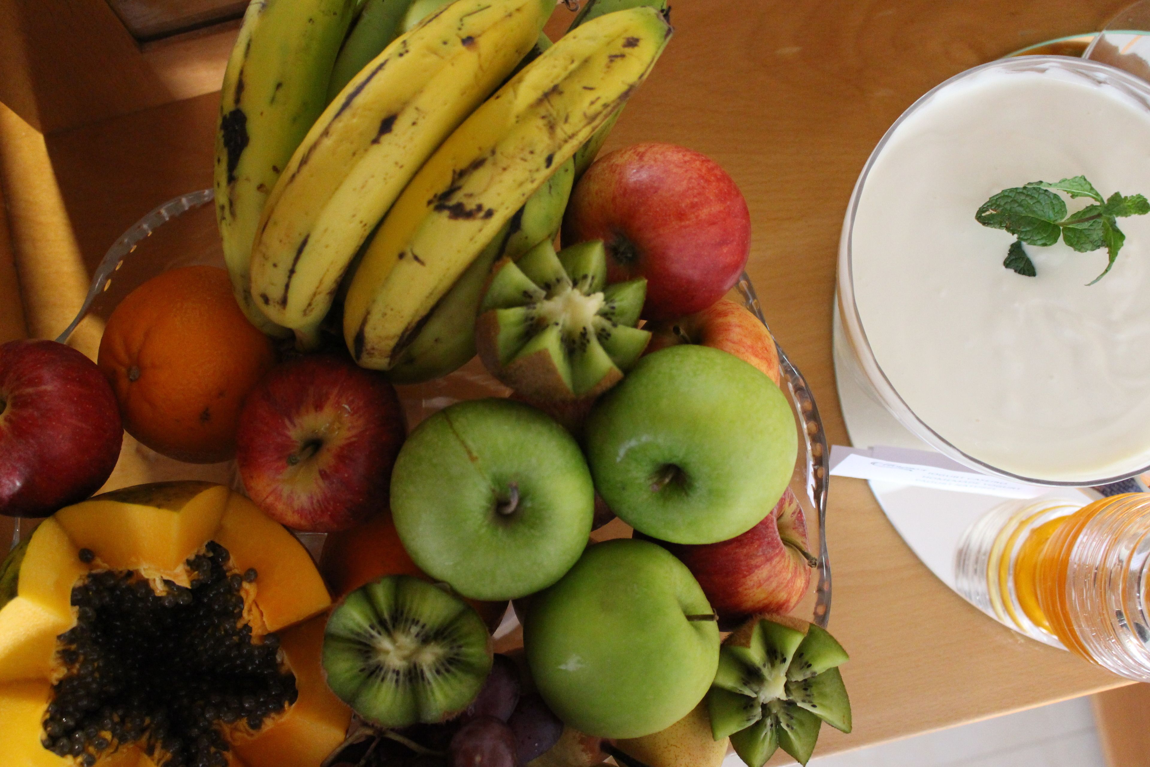 A fruit bowl with bananas, apples, and kiwi on a wooden table.