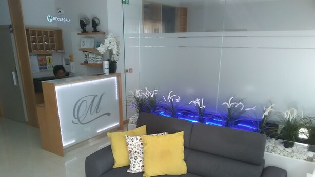 Un área de recepción con un mostrador, un sofá gris con cojines amarillos y un acuario montado en la pared con iluminación azul.