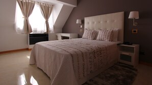 Un dormitorio con una cama grande, dos mesitas de noche, una lámpara de pared y un ventanal con cortinas.