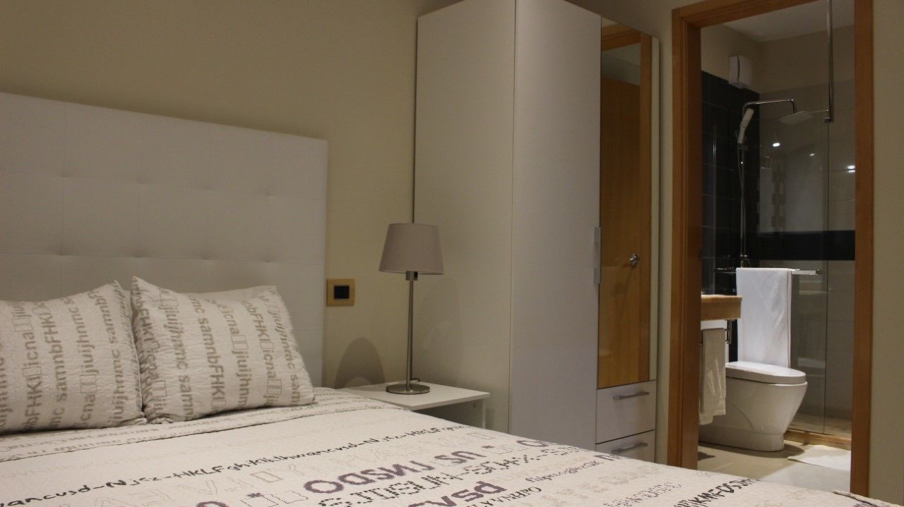 Ein Schlafzimmer mit Bett, Nachttisch mit Lampe, Kleiderschrank und einem Badezimmer mit Toilette und Dusche.