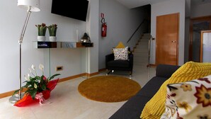 Una sala de estar moderna con una televisi ón de pantalla plana, un sofá, una mesa de centro y una escalera que lleva a otro piso.