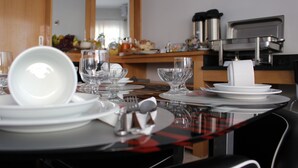 Una mesa de comedor dispuesta con platos blancos, vasos y cubiertos, con un camino de mesa a cuadros rojo y negro.