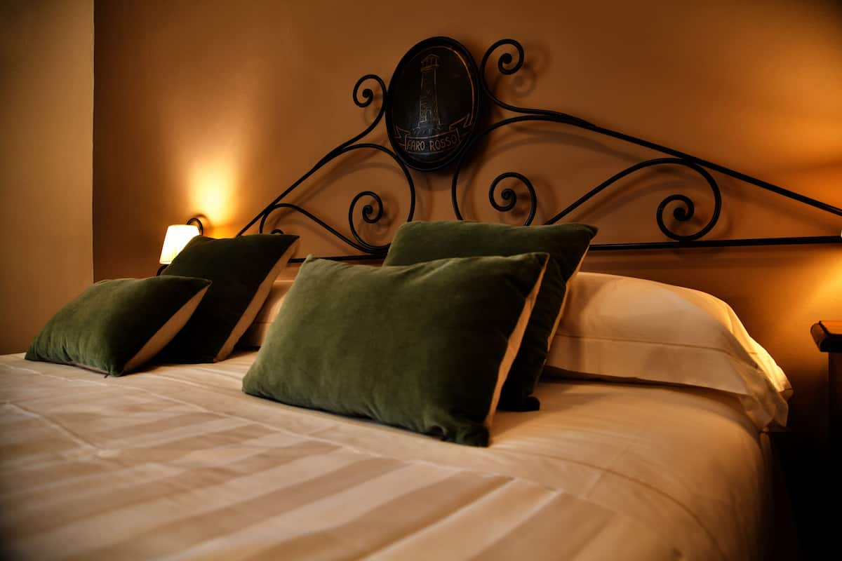 A neatly made bed with green pillows and a decorative wall piece above it.