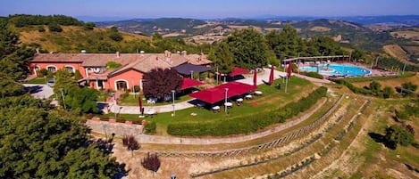 A large house with a swimming pool, surrounded by a landscaped garden and a terraced field.