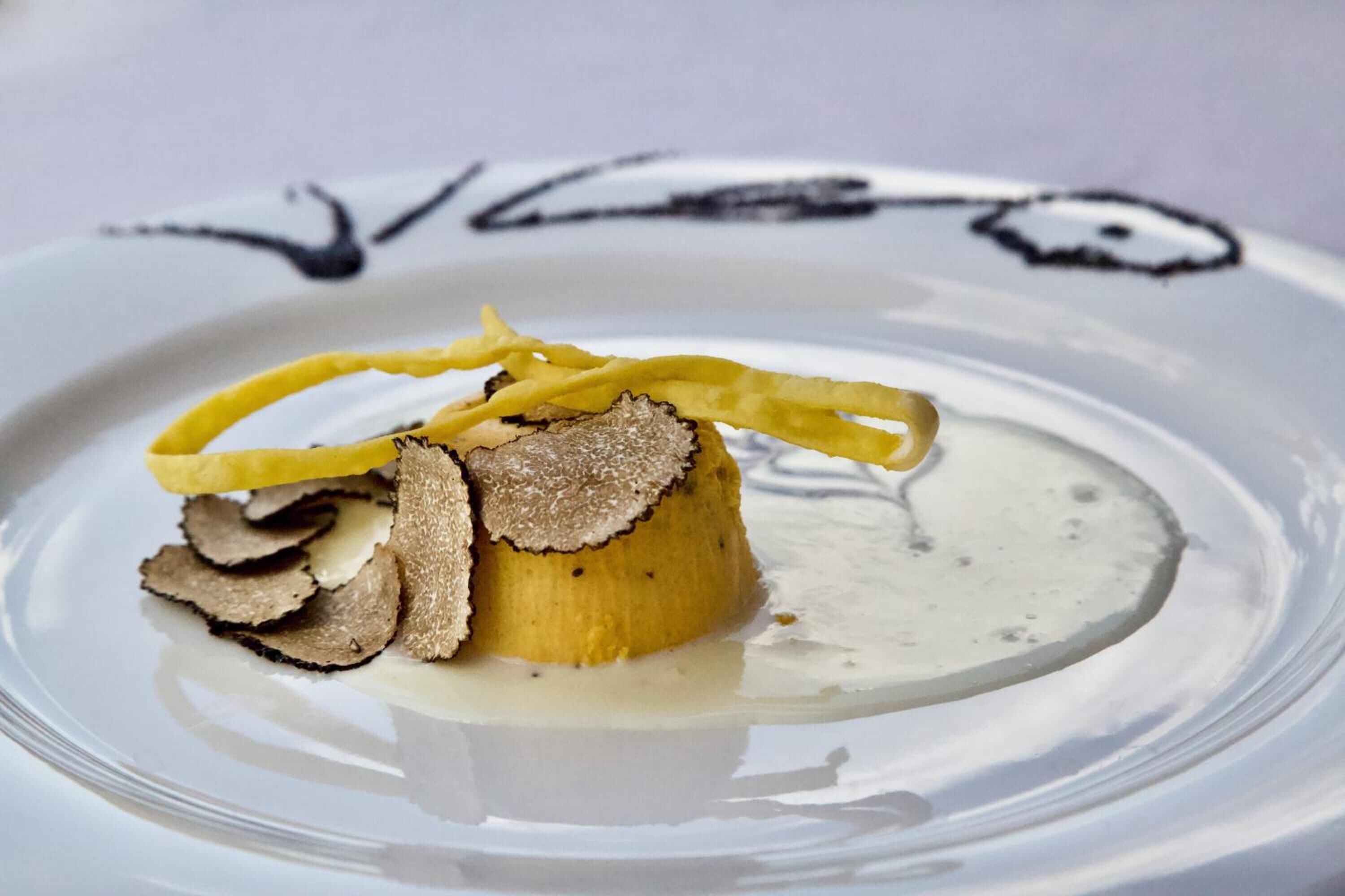 A plate with a food item, possibly a dessert, featuring a banana, truffle slices, and a yellow garnish.