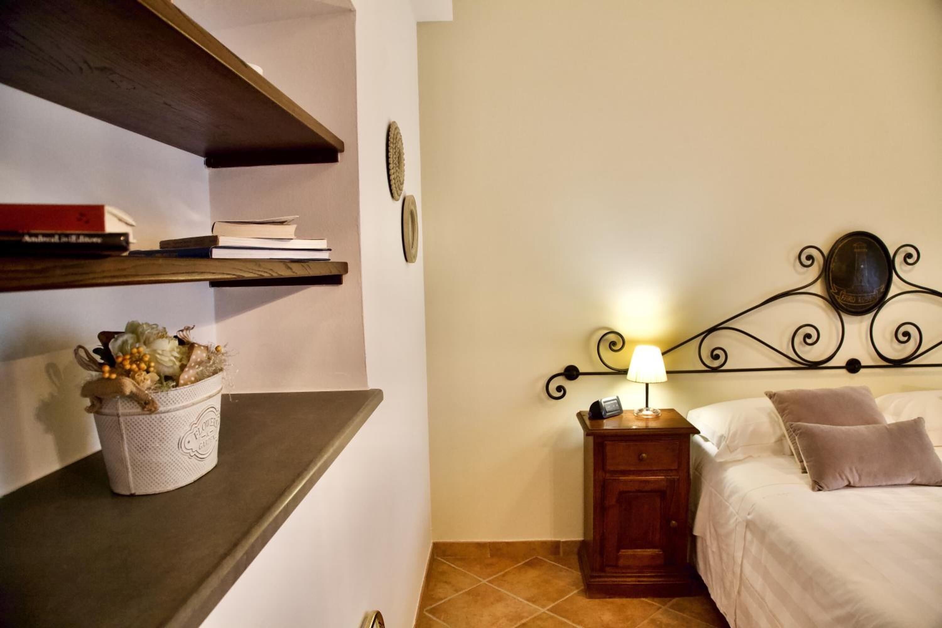 A bedroom with a bed, bedside table, lamp, and shelves with books and a decorative basket.