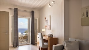 A modern living room with a desk, a sofa, and a view of the sea through an open door. - Selana Suites (Sifnos)