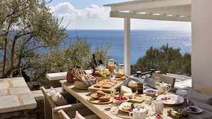 An outdoor dining area with a table set for breakfast, overlooking the sea. - Selana Suites (Sifnos)