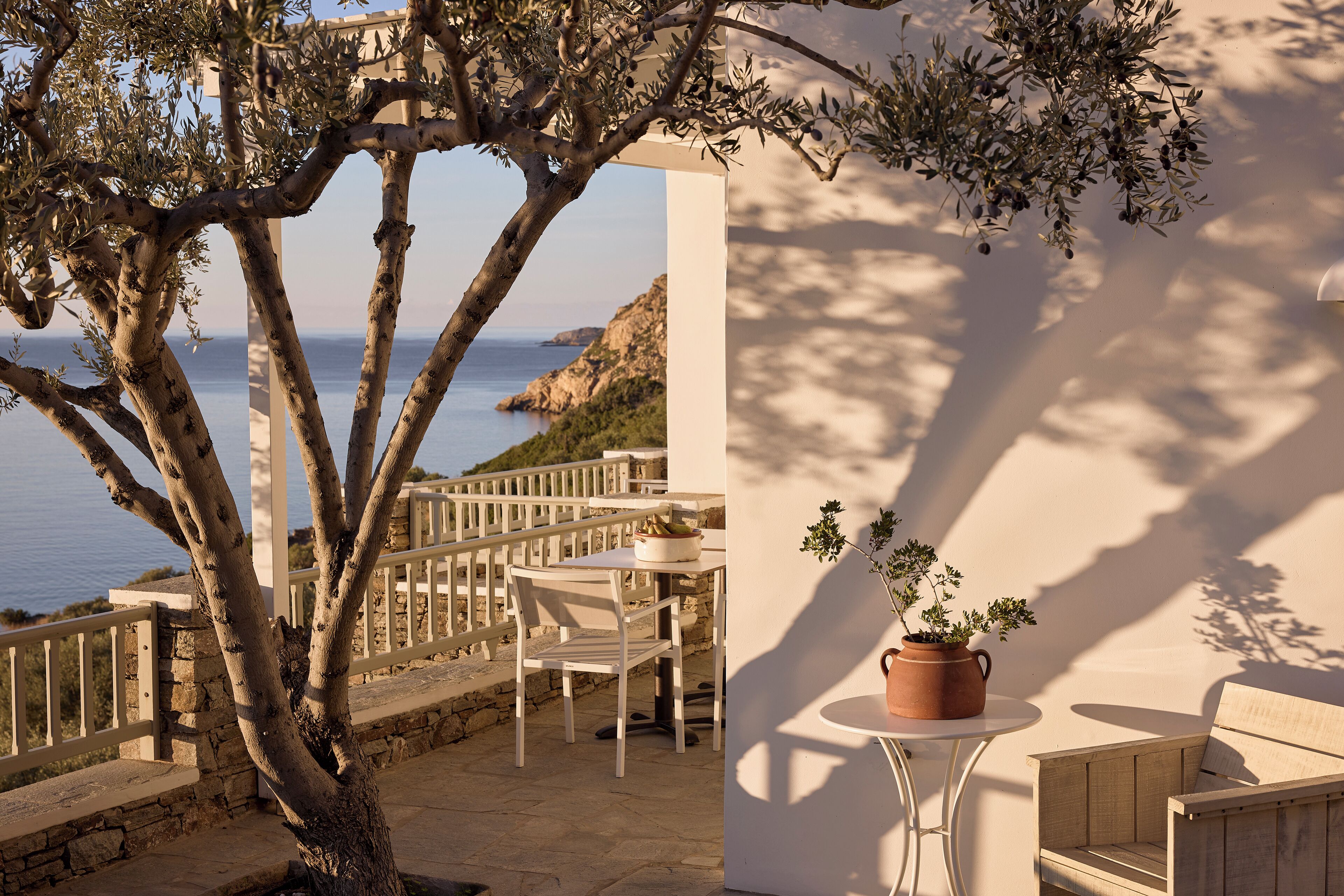 A terrace with a view of the sea, a white table, a chair, and a potted plant.