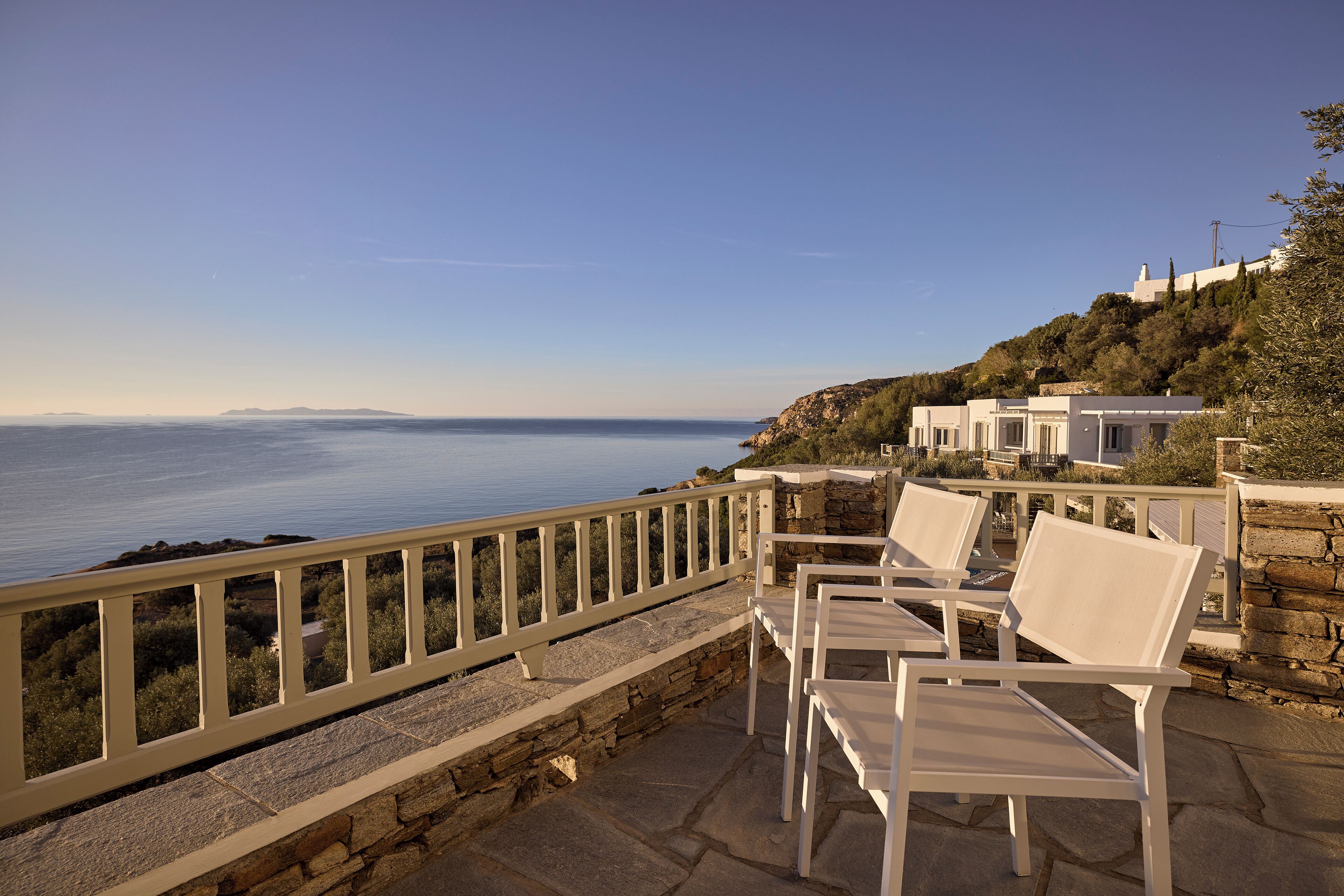 A terrace with white chairs overlooking a coastal view, stone steps, and a white railing.