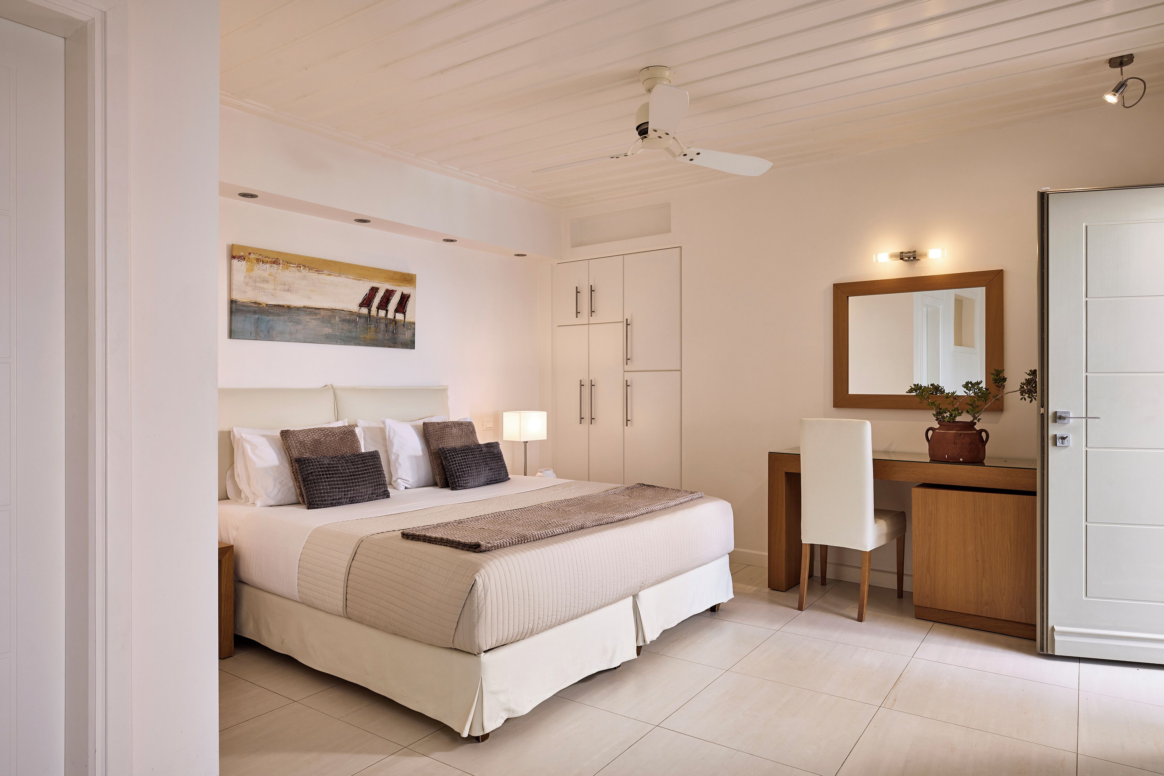 A bedroom with a bed, bedside table, desk, chair, wardrobe, and a ceiling fan.