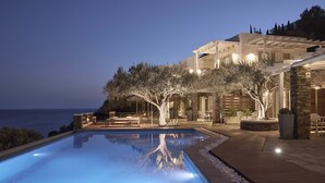 A swimming pool with a wooden deck, stone walls, and outdoor seating. - Selana Suites (Sifnos)