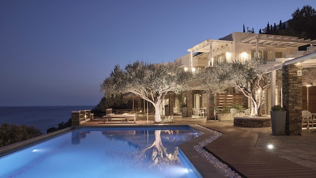 A swimming pool with a wooden deck, stone walls, and outdoor seating. - Selana Suites (Sifnos)