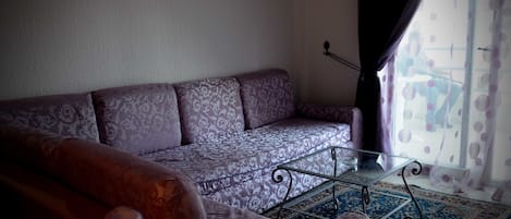 A living room with a patterned sofa, a glass coffee table, and a patterned rug.