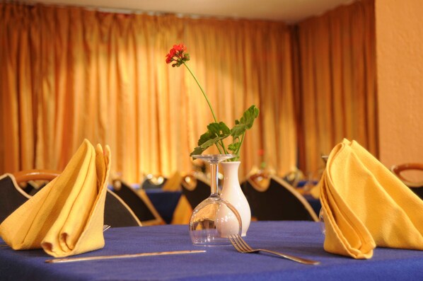 A table set with a clear glass vase containing a red flower, a white vase, and folded yellow napkins. - Residence Corail Royal Plage (Tabarka)