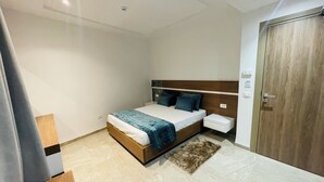 A bedroom with a bed, bedside tables, a nightstand, a wooden wardrobe, and a small rug. - Residence Corail Royal Plage (Tabarka)