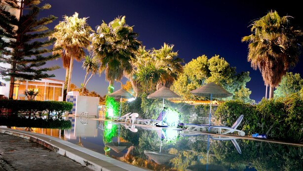 A nighttime pool area with palm trees, lounge chairs, and umbrellas. - Residence Corail Royal Plage (Tabarka)