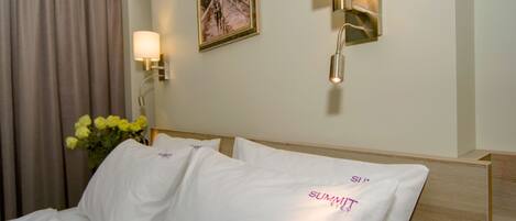 Habitación de hotel con una cama, almohadas blancas, un jarrón con flores amarillas y un cuadro en la pared.