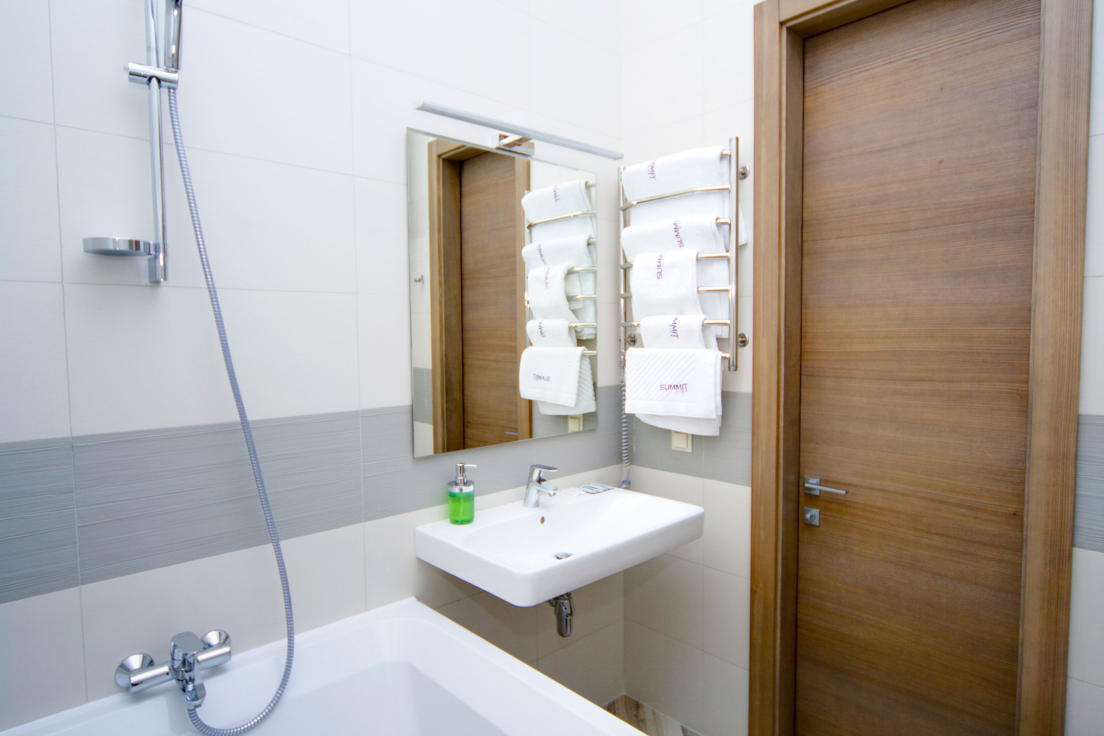 A bathroom with a white sink, a mirror, a shower, and a wooden door.