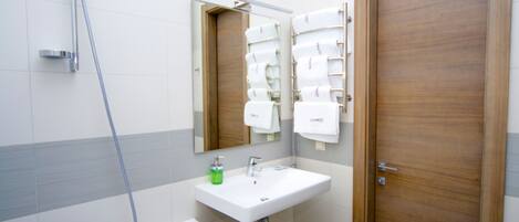 Un baño con lavamanos blanco, espejo, ducha y puerta de madera.
