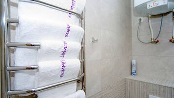 A bathroom with a towel rack holding four white towels, a showerhead, and a water heater.
