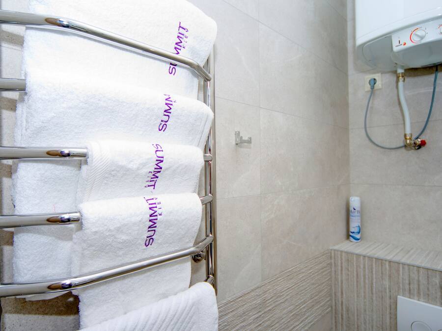 A bathroom with a towel rack holding four white towels, a showerhead, and a water heater.