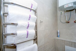 Un baño con un perchero que sostiene cuatro toallas blancas, un cabezal de ducha y un calentador de agua.