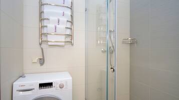 A modern bathroom with a Bosch washing machine, a glass shower enclosure, and a towel rack with towels labeled "SUMMIT".