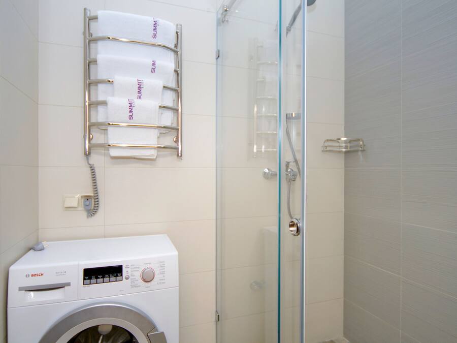 A modern bathroom with a Bosch washing machine, a glass shower enclosure, and a towel rack with towels labeled "SUMMIT".