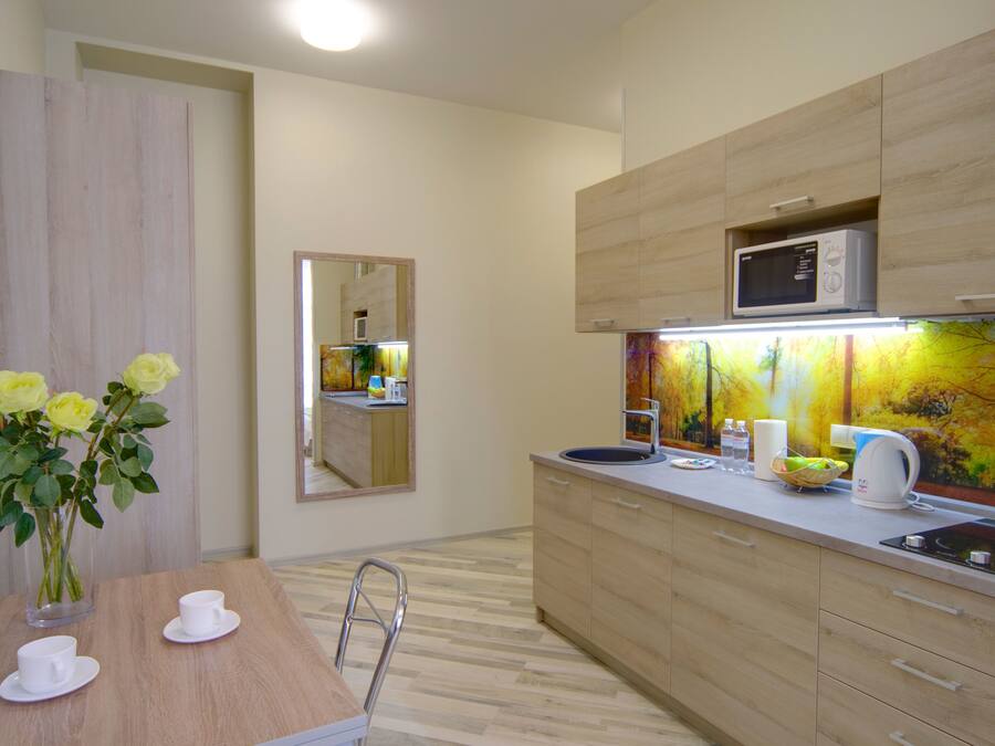 Una cocina moderna con armarios de madera, un microondas, una tetera y un florero con flores amarillas sobre la encimera.