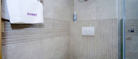 Un baño con inodoro blanco, un perchero con toalla blanca y zona de ducha con puerta de cristal.