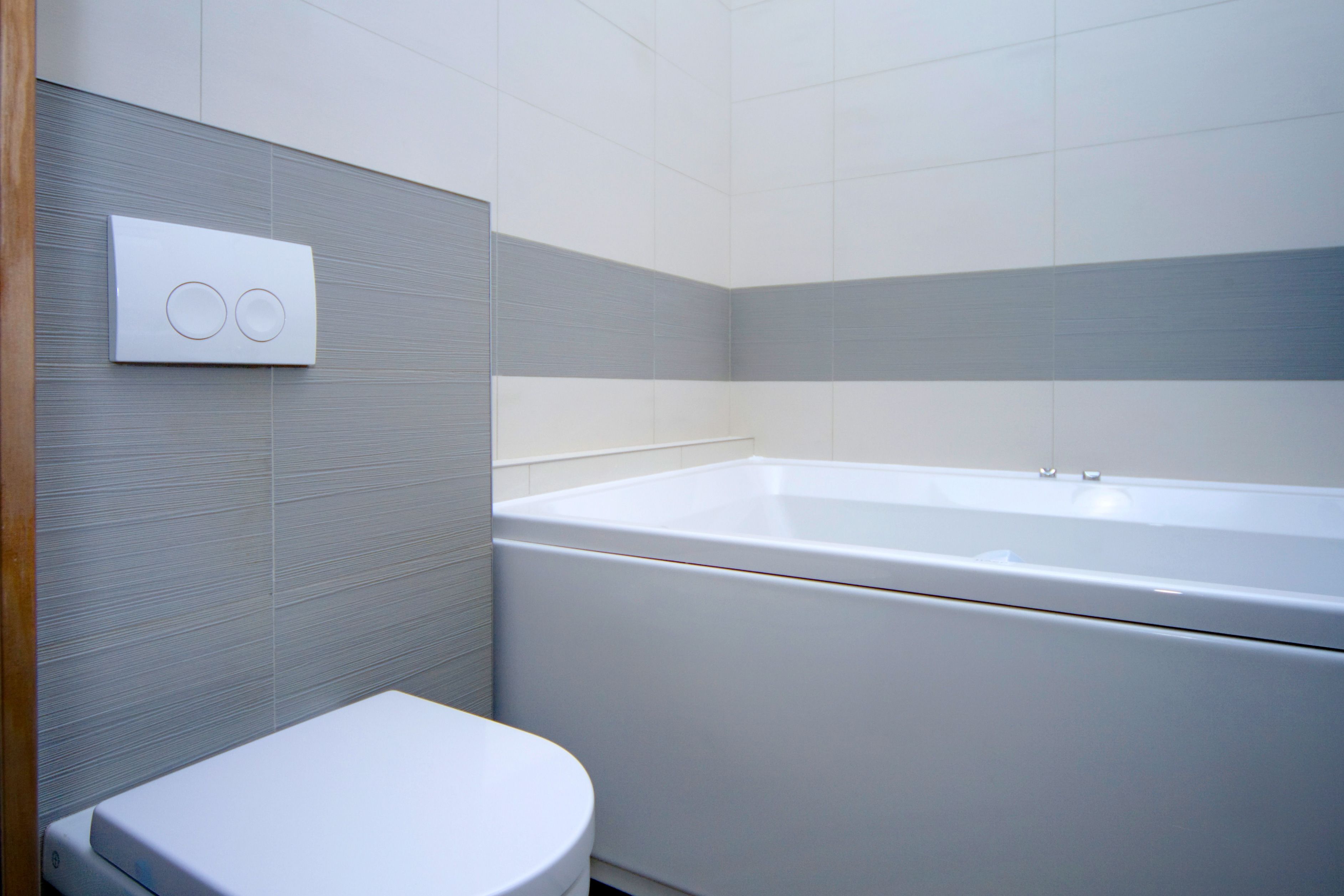 A modern bathroom with a white toilet, a bathtub, and a wall-mounted control panel.