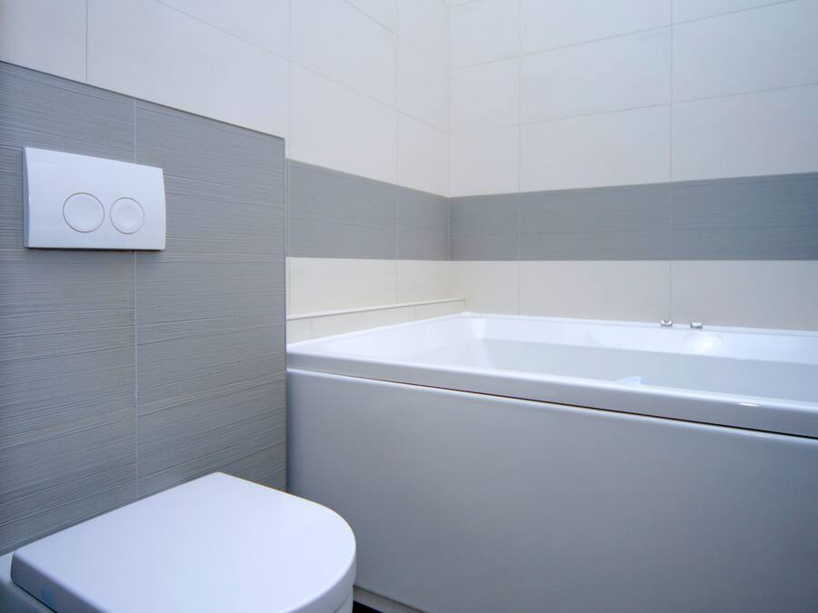 Un baño moderno con inodoro blanco, bañera y panel de control en la pared.