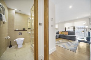 Un baño moderno con inodoro, lavamanos y ducha. Hay una sala de estar con sofá y vistas de la ciudad.