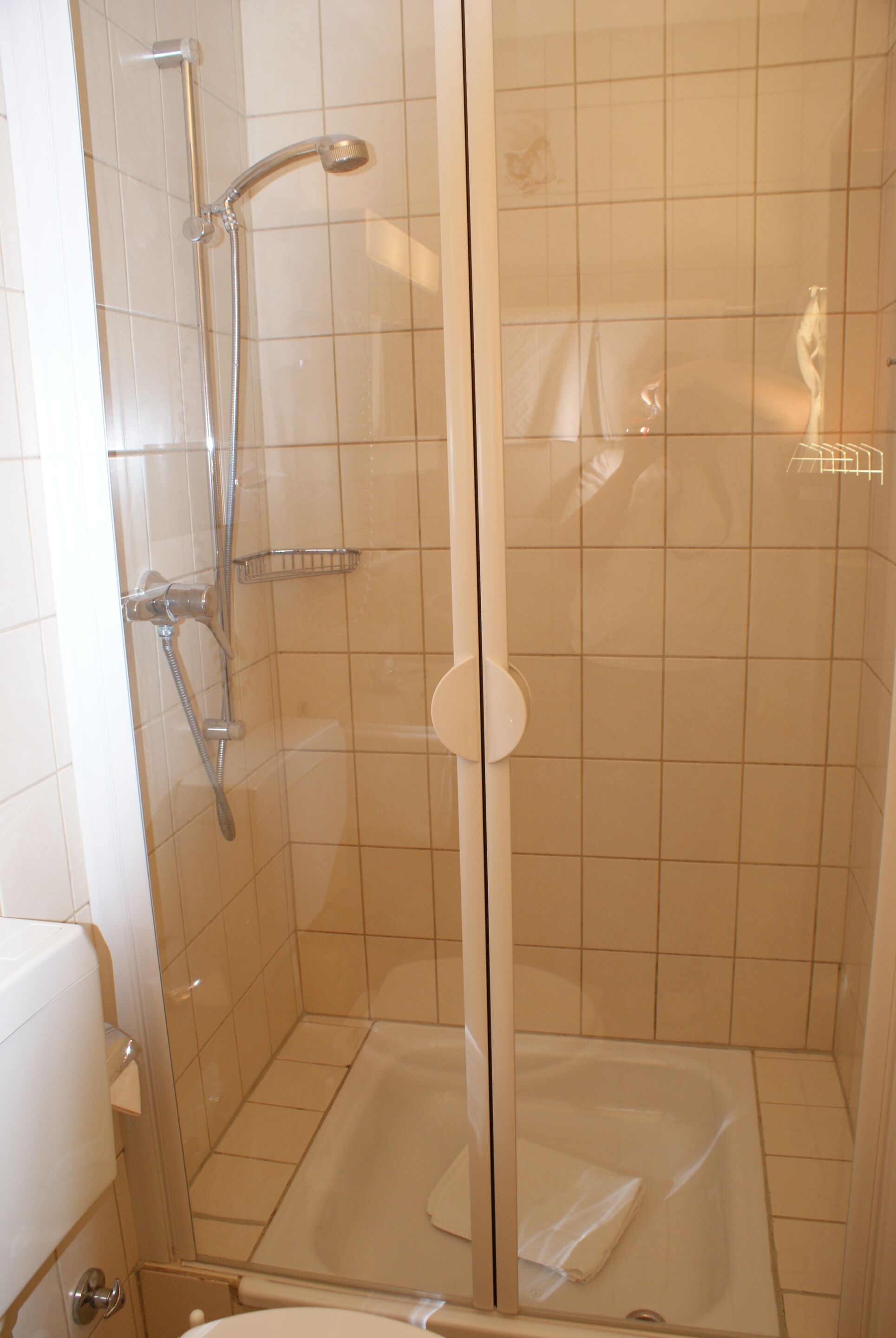 A glass-enclosed shower with a handheld showerhead, a handheld showerhead, and a glass-enclosed bathtub.