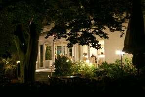 Un espace extérieur aménagé avec des tables et des chaises, entouré d’arbres et bordé d’un bâtiment doté de grandes fenêtres.