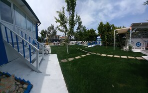 A residential area with a blue and white building, a grassy lawn, and outdoor seating. - Hotel Antonio (Cesme)