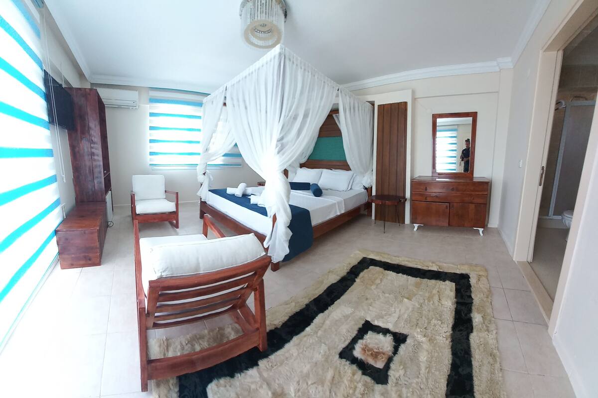 A bedroom with a four-poster bed, a wooden chair, a small table, and a mirror.