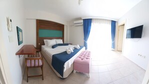 A hotel room with a bed, a desk, a chair, a TV, and a bathroom visible through a door. - Hotel Antonio (Cesme)