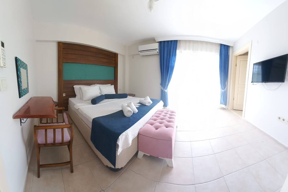 A hotel room with a bed, a desk, a chair, a TV, and a bathroom visible through a door.
