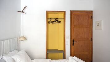A hotel room with a bed, a hanging light fixture, a wooden door, and a coat rack with hangers.