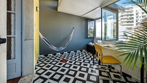 Una habitación con una hamaca, una silla amarilla, un escritorio y un ventanal con vistas a edificios.