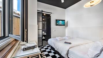 Een moderne hotelkamer met een geruit vloerkleed, een bed met witte lakens, een klein tafeltje met een boek en een televisie aan de muur.