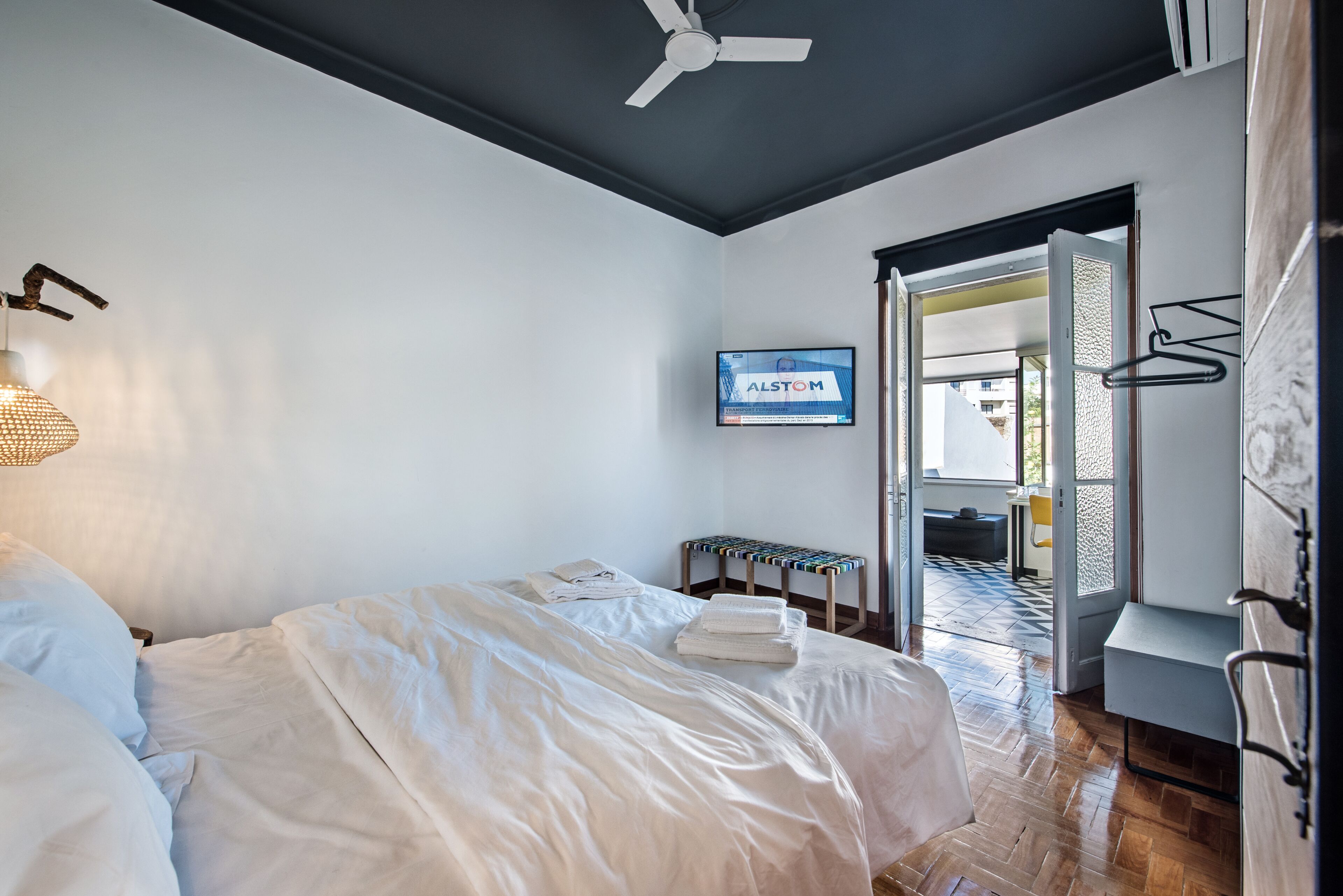 A hotel room with a bed, a ceiling fan, a TV, and a view of the outside.