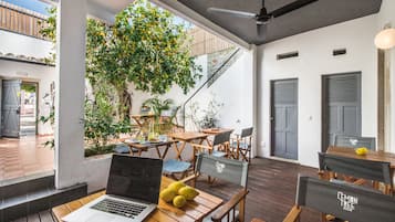 Un área de comedor exterior moderna con mesas y sillas de madera, una computadora portátil y limones sobre una mesa.