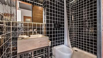 A modern bathroom with black tiled walls, a wooden vanity, and a white toilet.